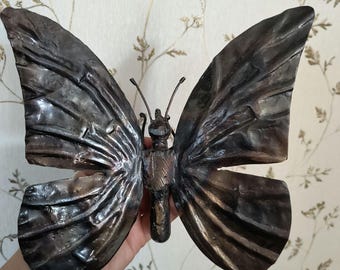 May include: A metal butterfly sculpture with a dark brown finish. The wings are textured and have a slightly iridescent sheen.