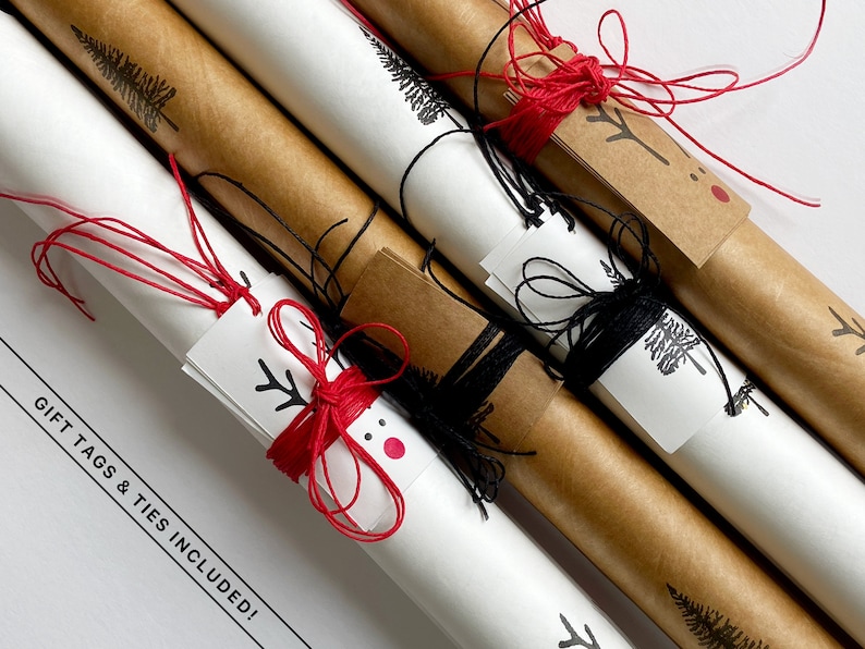 May include: Three rolls of brown kraft paper wrapping paper with white paper printed with black trees and a reindeer design. Each roll is tied with red or black twine and includes a matching gift tag with a reindeer design. The text "GIFT TAGS & TIES INCLUDED!" is printed on the white surface.
