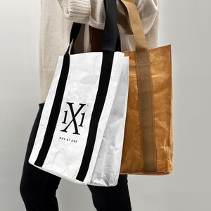 May include: Two reusable shopping bags, one white with black stripes and the logo "1X1 ONE BY ONE", and one brown with tan straps.