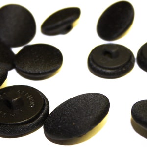 May include: A collection of black buttons with a textured finish. Some buttons have a shank, while others have a flat back with two holes.