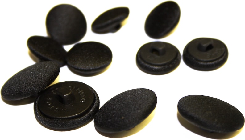 May include: A collection of black buttons with a textured finish. Some buttons have a shank, while others have a flat back with two holes.