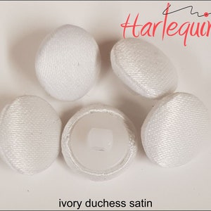 May include: Five white ivory duchess satin buttons. The buttons are round and have a smooth, shiny finish.