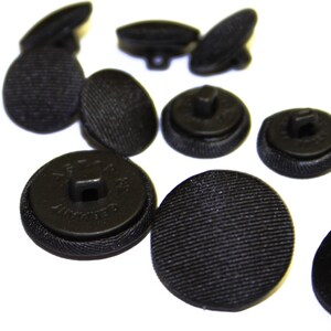 May include: A group of 10 black buttons with a textured surface. The buttons are round and have a flat back. Some of the buttons have a shank, while others have a hole.