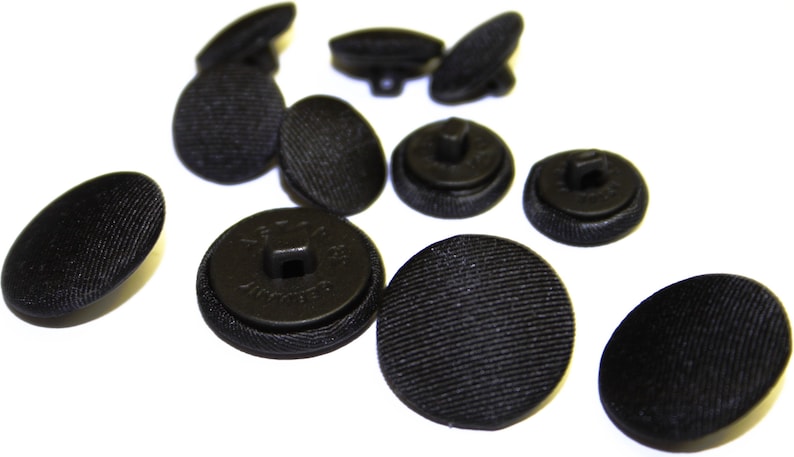May include: A group of 10 black buttons with a textured surface. The buttons are round and have a flat back. Some of the buttons have a shank, while others have a hole.