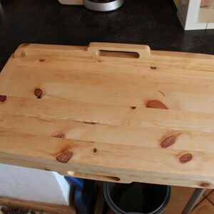 May include: A large, rectangular wooden chopping board with a handle. The board is made of light wood with a natural finish. It has a slightly rounded edge and a small hole in the bottom for hanging.