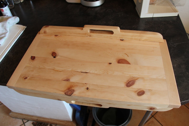 May include: A large, rectangular wooden chopping board with a handle. The board is made of light wood with a natural finish. It has a slightly rounded edge and a small hole in the bottom for hanging.