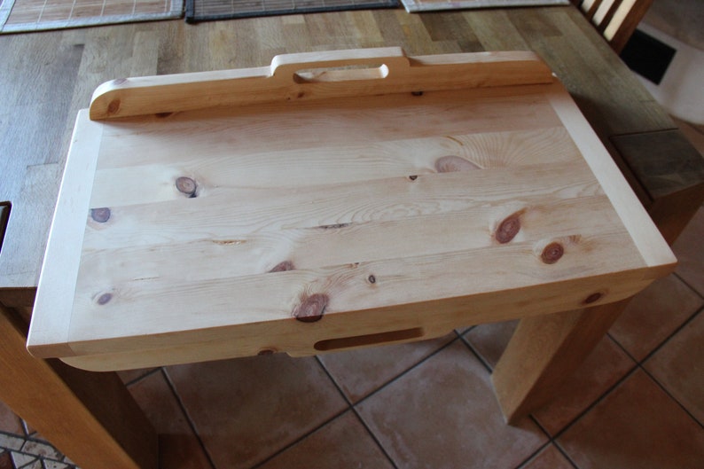 May include: A light wood serving tray with a handle and two cutouts on the underside. The tray is made of natural wood with knots and grain patterns.