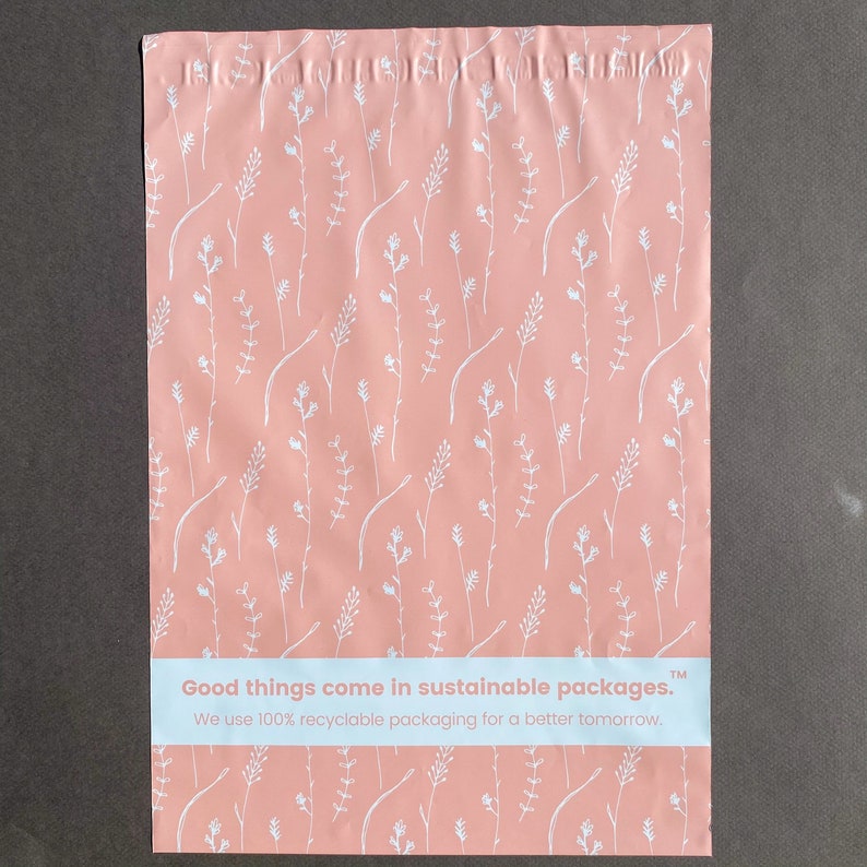 K&ouml;nnte beinhalten: Rosa Poly-Versandtaschen mit einem wei&szlig;en Blumenmuster. Die Versandtaschen haben ein wei&szlig;es Etikett mit dem Text "Good things come in sustainable packages. TM We use 100% recyclable packaging for a better tomorrow."