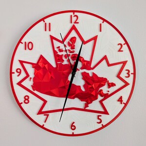 Peut inclure: Une horloge murale ronde avec un motif de feuille d'érable rouge et un fond blanc. L'horloge a des chiffres rouges, un bord rouge et des aiguilles noires. Le centre représente le Canada en rouge.