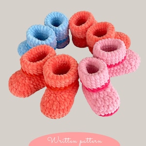 Może przedstawiać: Sześć par szydełkowych bucików dla niemowląt w kolorze różowym, koralowym i niebieskim. Buciki są wykonane z puszystej przędzy i mają prosty wzór.