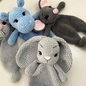 May include: A collection of handmade crochet stuffed animals in various shapes. The toys include a blue hippo, two gray mice with pink ears, a gray bunny with long ears, and a gray mouse. The toys are made of soft, plush yarn.