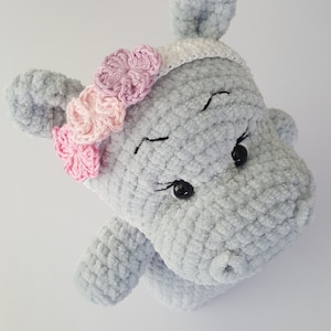 Op de afbeelding: Een grijs gehaakt nijlpaard speelgoed met zwarte ogen en een roze en paarse bloemenhoed.