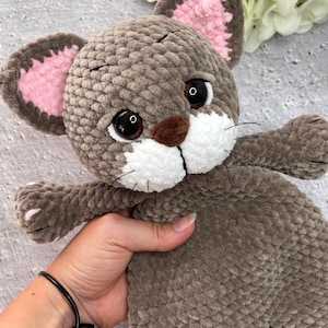 May include: A handmade plush cat toy in shades of brown, with pink inner ears and white accents on the muzzle. The cat has large, expressive eyes and black whiskers. The toy is soft and cuddly, perfect for children.