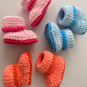 May include: Three pairs of crocheted baby booties in pink, blue, and orange. Each bootie has a contrasting colored trim around the top.