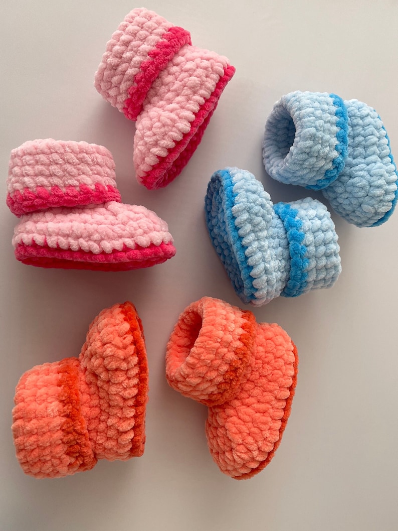 May include: Three pairs of crocheted baby booties in pink, blue, and orange. Each bootie has a contrasting colored trim around the top.