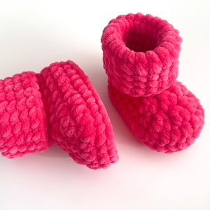 May include: A pair of pink crocheted baby booties with a fuzzy texture.