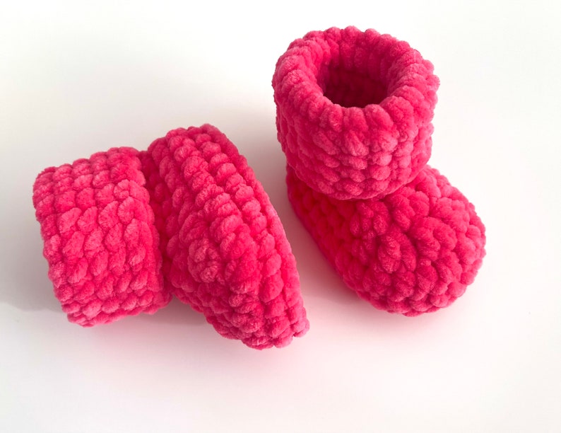 May include: A pair of pink crocheted baby booties with a fuzzy texture.