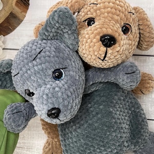 Puede incluir: Dos juguetes de peluche con forma de perro. Uno es gris con ojos azules y nariz negra, el otro es marrón con ojos marrones y nariz negra. Ambos tienen detalles cosidos y están hechos de un material suave y texturizado.