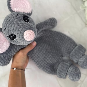 Könnte beinhalten: Ein graues, gehäkeltes Maus-Stofftier mit weicher, samtiger Textur. Die Maus hat große, runde Ohren mit hellrosa Innenseiten, eine kleine rosa Nase und schwarze Sicherheitsaugen aus Kunststoff mit aufgestickten Wimpern.