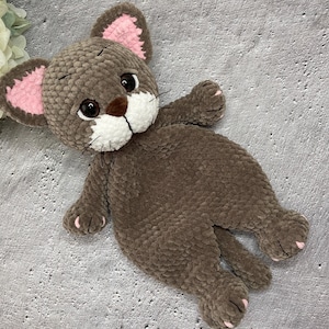 May include: A handmade brown plush cat toy with pink inner ears, white muzzle, and black eyes. The cat has a soft, textured appearance and is lying down. The toy is a cuddly, child-friendly item.
