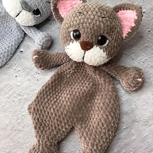 May include: Two handmade crochet animal toys. One is gray, the other is brown. The brown toy has a lion-like appearance with a brown snout, white muzzle, and pink inner ears. The gray toy has a similar design. Both toys are soft and plush.