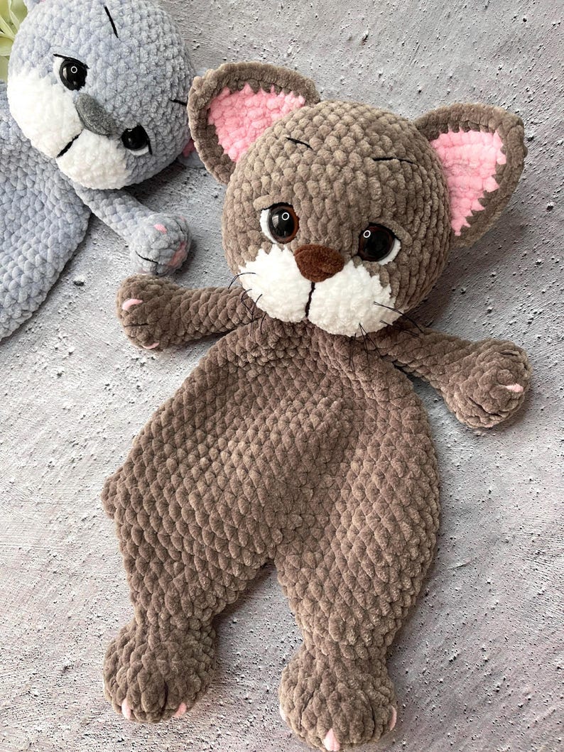 May include: Two handmade crochet animal toys. One is gray, the other is brown. The brown toy has a lion-like appearance with a brown snout, white muzzle, and pink inner ears. The gray toy has a similar design. Both toys are soft and plush.