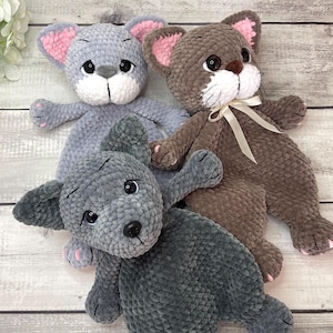 May include: Three handmade crochet stuffed animals: a gray mouse with pink ears, a brown cat with a cream bow, and a gray dog. Each plush toy has black eyes and pink paw pads.