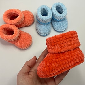 May include: Three pairs of crocheted baby booties. Two pairs are a light blue color and one pair is a bright orange color.