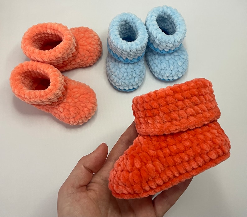 May include: Three pairs of crocheted baby booties. Two pairs are a light blue color and one pair is a bright orange color.