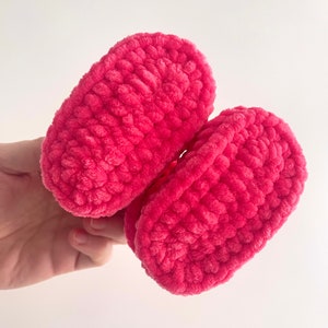 May include: A pair of pink crocheted baby booties. The booties are made with a soft, fuzzy yarn and have a simple, classic design.