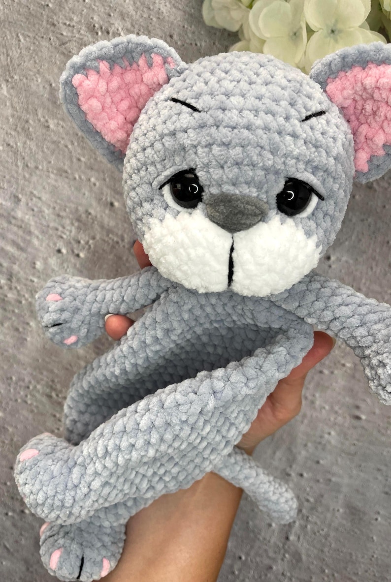 May include: A handmade gray crochet mouse plush toy with pink inner ears and paw pads. The mouse has black eyes and a white muzzle. The toy is soft and cuddly, perfect for children.