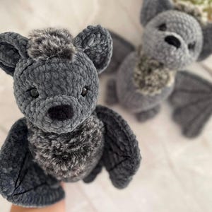 Könnte beinhalten: Zwei Plüschfledermaus-Spielzeuge in Grau. Die Fledermäuse haben große Ohren, Flügel und eine pelzige Brust. Die Spielzeuge bestehen aus einem weichen, strukturierten Material. Eine Fledermaus ist im Fokus, die andere ist leicht verschwommen im Hintergrund.