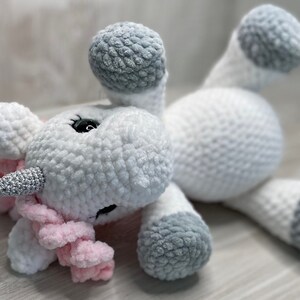 May include: A white crocheted unicorn plush toy with a pink mane and tail. The unicorn has a silver horn and gray hooves.