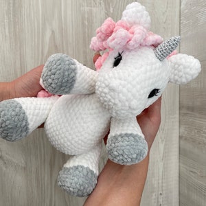 May include: A white crocheted unicorn stuffed animal with pink yarn for the mane and horn, and gray yarn for the hooves.