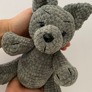 Pu&ograve; includere: Un cane di peluche grigio lavorato a uncinetto con occhi neri e naso nero.