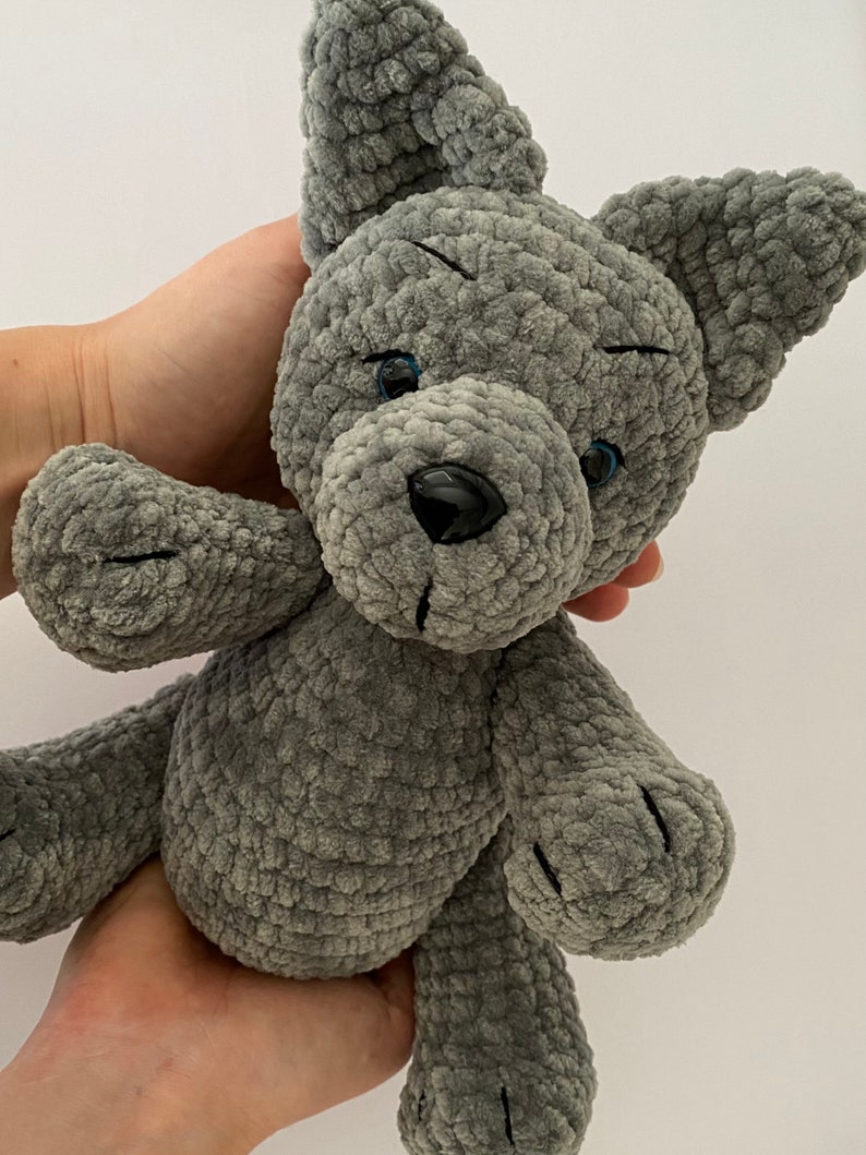 Pu&ograve; includere: Un cane di peluche grigio lavorato a uncinetto con occhi neri e naso nero.
