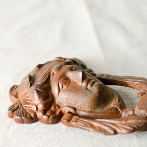 May include: A rusty brown metal door knocker shaped like a woman's face with a crown. The knocker has a ring handle and intricate details.