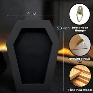 May include: A black coffin-shaped display box measuring 4 inches wide by 5.3 inches tall. It features a brass hook hanger, a clear acrylic front panel, and is constructed from fine pine wood. The interior is matte black with a deep recessed area.