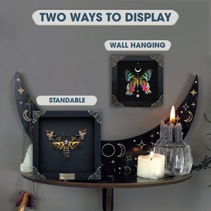 May include: Two square black shadow box frames with ornate metal corner accents. One frame displays a Death's-head hawkmoth, the other a colorful butterfly. Text reads: TWO WAYS TO DISPLAY, WALL HANGING, and STANDABLE.
