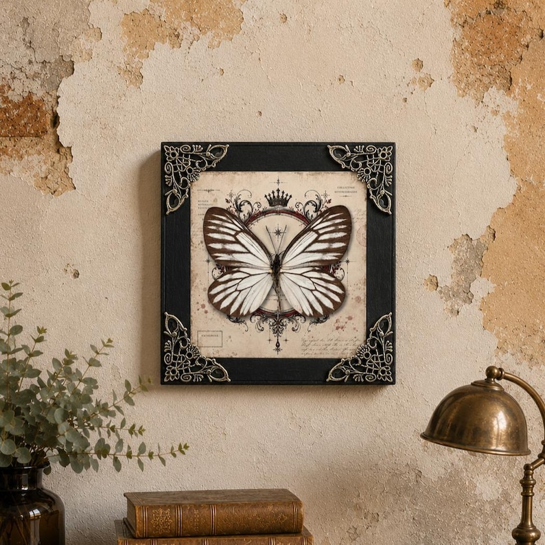 May include: A square wall art piece featuring a central illustration of a white and brown butterfly with striped wings. The artwork is set within a black frame adorned with ornate, metallic silver-toned corner accents and a crown motif.