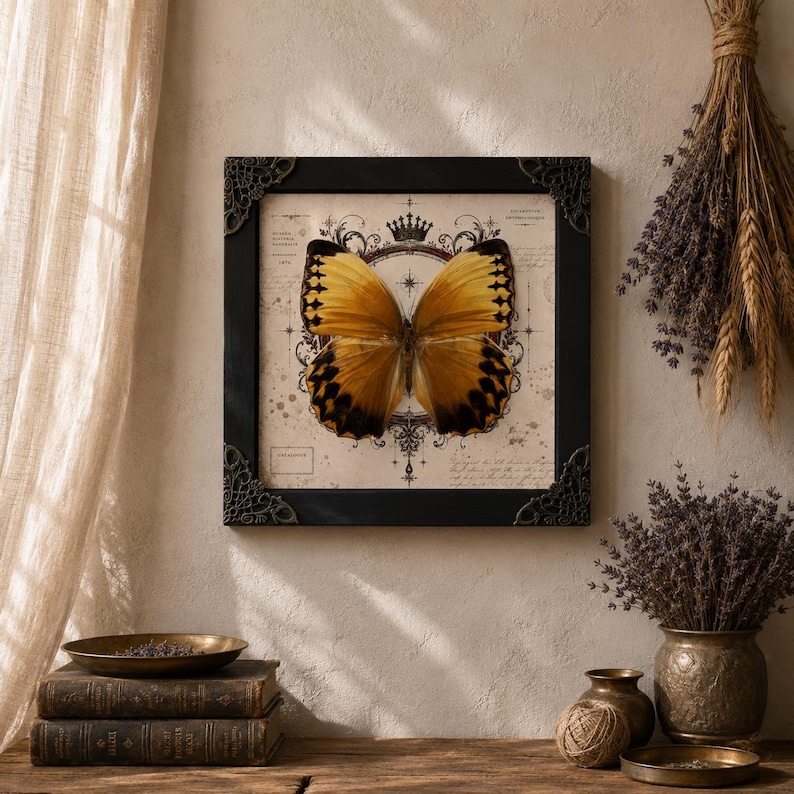 May include: A square framed wall art piece featuring a large, golden-yellow butterfly with dark brown wing edges. The butterfly is centered over a vintage-style background with a crown icon, compass-like markings, and faint cursive script text.