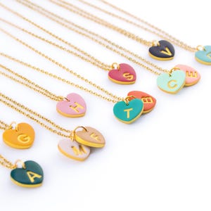 May include: A set of gold necklaces with heart-shaped pendants featuring different letters of the alphabet. Each heart is a different colour, including pink, green, yellow, and blue.