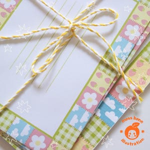 May include: A bundle of stationery tied with yellow and white twine. The stationery features a patterned border with flowers, strawberries, and gingham. The paper is white with green lines. The illustration includes a logo with the text "moss bone illustration".