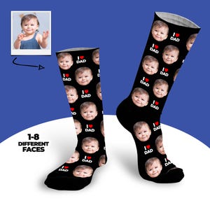 May include: Black socks featuring a repeating pattern of a baby's face and the text "I ❤️ DAD" in white and red. A small photo of the baby is in the upper left corner. The text "1-8 DIFFERENT FACES" is also visible.
