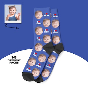 May include: Blue socks featuring multiple baby faces and the text "I ❤️ MOM." The socks have a black heel and toe. A small photo of a baby is in the upper left corner. The text "1-8 DIFFERENT FACES" is in the lower left corner.