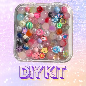 May include: A clear plastic container filled with colourful beads. The beads are various shapes and sizes, including stars, hearts, and smiley faces. The container is labelled "DIY KIT".