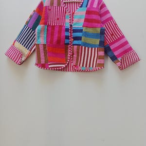 Può includere: Giacca patchwork colorata con scollo a V e maniche lunghe. La giacca presenta varie toppe di tessuto nei toni del rosa, rosso, blu e viola. È abbottonata e ha una texture trapuntata.