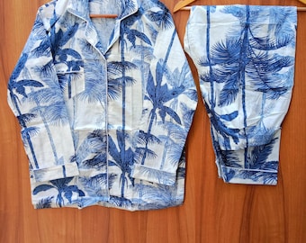 May include: A white pyjama set with a blue palm tree print. The top has a button-up front and long sleeves. The trousers are long and have a straight leg.