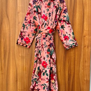 Peut inclure: Une robe en velours rose avec un imprim&eacute; floral et d'oiseaux. La robe a une ceinture &agrave; nouer et des manches longues.