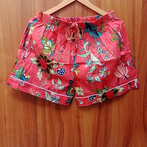 May include: Red cotton shorts with a floral print and white trim. The shorts have a drawstring waist.